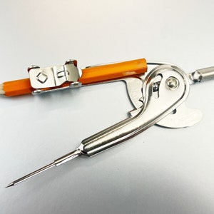Puede incluir: Un compás plateado con un lápiz naranja adjunto. El compás tiene una punta de metal y un dial giratorio.