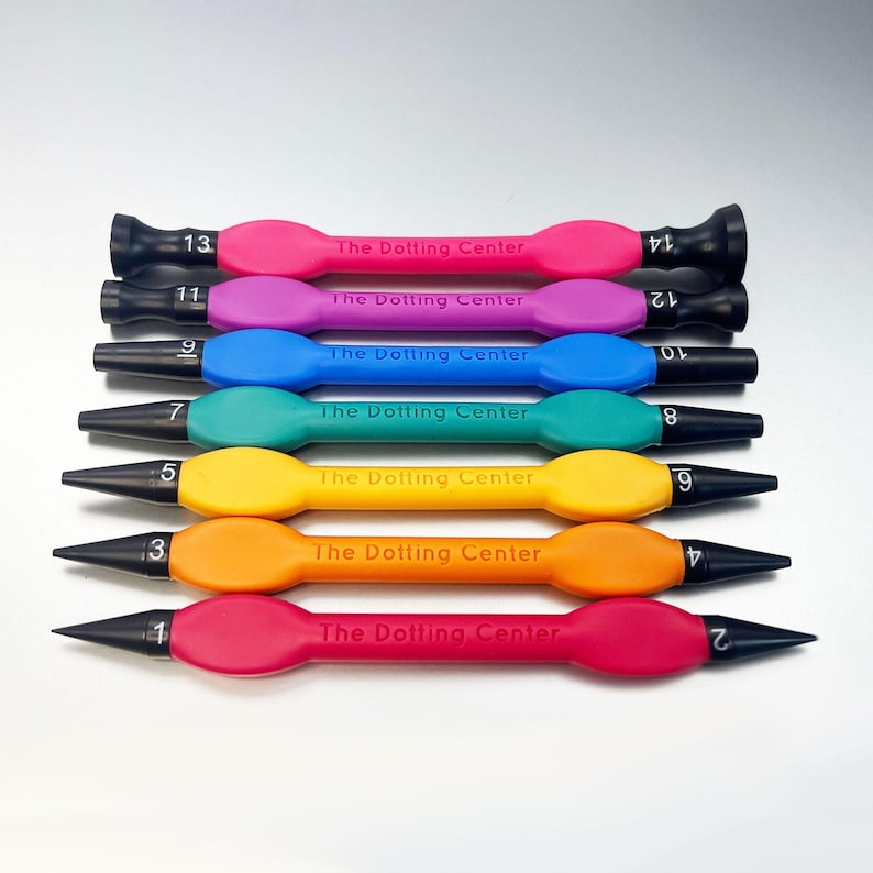 Puede incluir: Conjunto de 7 herramientas de punteado de colores con puntas negras, numeradas del 1 al 13. Cada herramienta tiene impreso "The Dotting Center".