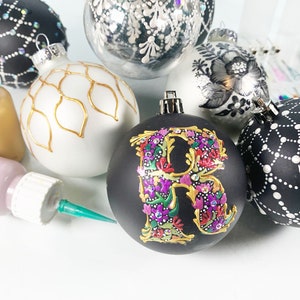 May include: A collection of six hand-painted Christmas ornaments. The ornaments are all different colors and designs, including black and white, gold and white, and silver and black. The ornaments are decorated with various patterns, including dots, lines, and floral designs. The ornaments are perfect for adding a touch of elegance to your Christmas tree.
