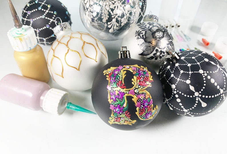 May include: A collection of six hand-painted Christmas ornaments. The ornaments are all different colors and designs, including black and white, gold and white, and silver and black. The ornaments are decorated with various patterns, including dots, lines, and floral designs. The ornaments are perfect for adding a touch of elegance to your Christmas tree.