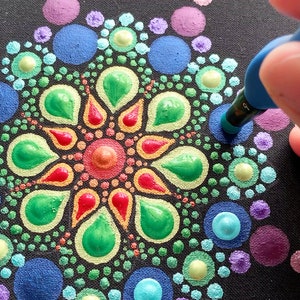 Puede incluir: Primer plano de una mano usando una herramienta de punteado azul para crear un mandala colorido en un lienzo negro. El mandala est&aacute; hecho de peque&ntilde;os puntos de varios colores, incluyendo morado, azul, verde, amarillo, naranja y rojo. La herramienta est&aacute; etiquetada como "TOOL 9".
