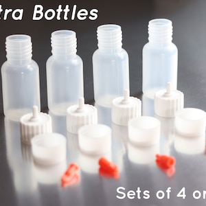 May include: Set of four clear plastic bottles with white dropper caps. The bottles are labeled "Extra Bottles" and "Sets of 4 or 8".