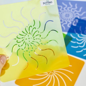 May include: Four colorful plastic stencils with a swirling sun design. The stencils are yellow, blue, orange, and purple. The text "The Dotting Center" is printed on the yellow stencil.