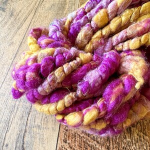 Puede incluir: Primer plano de un ovillo de hilo en tonos rosa y amarillo. El hilo es suave y esponjoso, perfecto para tejer o hacer ganchillo.