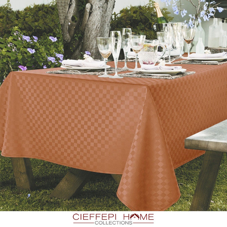 Pode incluir: Uma toalha de mesa laranja xadrez colocada em uma mesa de madeira com copos e pratos. A toalha de mesa &eacute; feita de um tecido macio e tecido. A mesa est&aacute; posta para uma refei&ccedil;&atilde;o ao ar livre em um jardim.