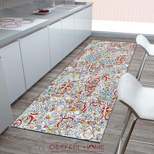 May include: A colorful kitchen runner rug with a patterned design of tiles. The rug is white with red, blue, green, and yellow accents. The rug is placed on a wood floor in a kitchen.