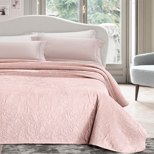 Può includere: Un copriletto trapuntato rosa con un motivo floreale. Il copriletto è su un letto con cuscini bianchi e rosa.