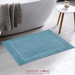 Può includere: Un tappetino da bagno blu chiaro con un bordo bianco. Il tappetino è realizzato in cotone morbido e assorbente ed è perfetto per asciugare i piedi dopo la doccia o il bagno.