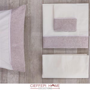 Puede incluir: Juego de cama blanco con un borde decorativo con diseño moteado en color lila claro. El juego incluye una funda de almohada, una sábana doblada y una manta doblada. La marca "CIEFFEPI HOME COLLECTIONS" es visible.