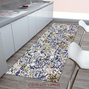May include: A blue, yellow, and green patterned kitchen runner rug with a white background. The rug has a geometric design and is made of a soft, durable material. The rug is placed in a kitchen with white cabinets and a stainless steel sink.