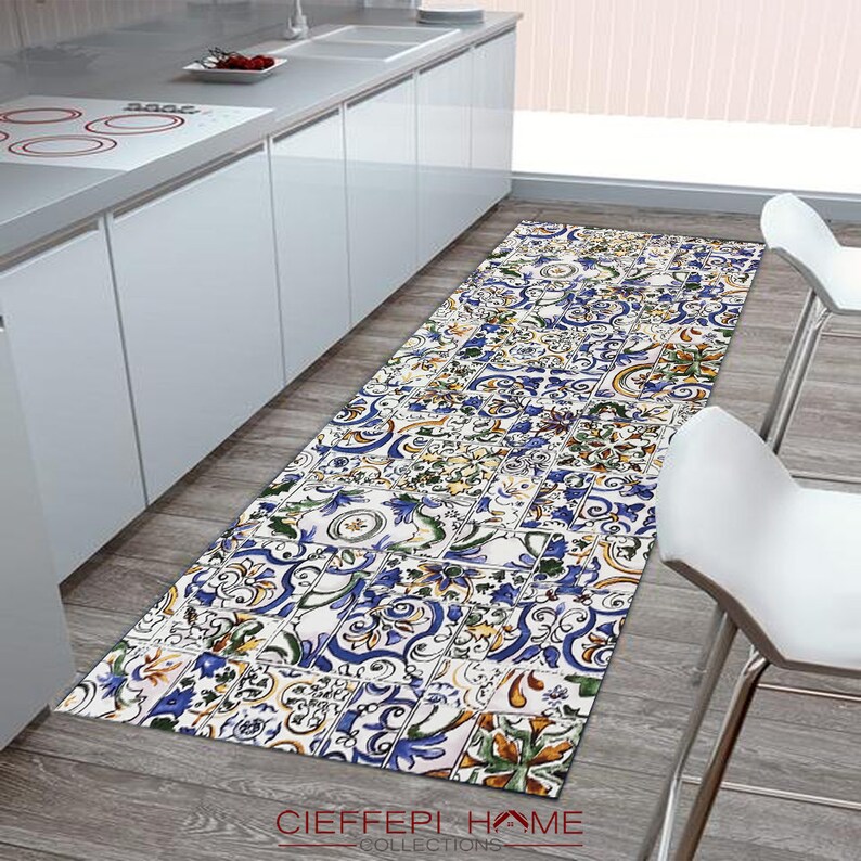 May include: A blue, yellow, and green patterned kitchen runner rug with a white background. The rug has a geometric design and is made of a soft, durable material. The rug is placed in a kitchen with white cabinets and a stainless steel sink.