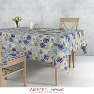 Peut inclure: Une nappe beige avec un motif floral bleu et blanc. La nappe est drapé sur une table en bois avec deux chaises en bois.