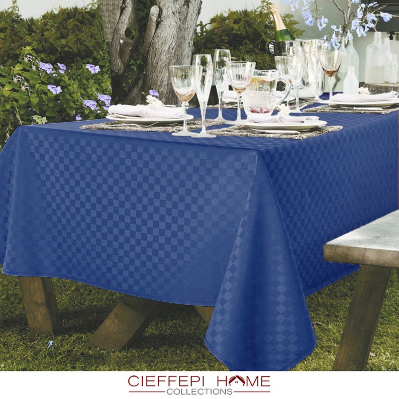 Pode incluir: Uma toalha de mesa quadriculada azul com um padr&atilde;o quadriculado, colocada em uma mesa de madeira com copos e um jarro. A toalha de mesa &eacute; feita de um tecido macio e tecido e tem um brilho sutil. A toalha de mesa &eacute; perfeita para uma experi&ecirc;ncia informal de jantar ao ar livre.