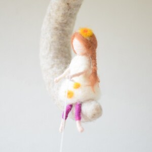 May include: A felt doll with brown hair and a white dress with yellow flowers. The doll is wearing purple pants and has a yellow flower crown.