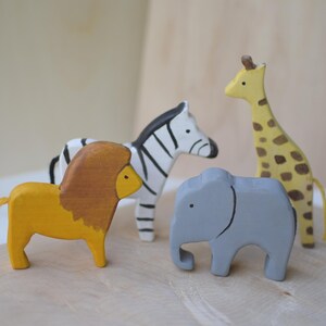 Peut inclure: Ensemble de jouets en bois représentant un lion jaune avec une crinière marron, un zèbre rayé noir et blanc, un éléphant gris et une girafe jaune avec des taches marron.