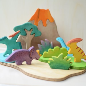May include: Wooden dinosaur toy set featuring a volcano, trees, and various dinosaurs in shades of green, blue, purple, orange, and yellow. The set is designed for imaginative play and educational purposes.
