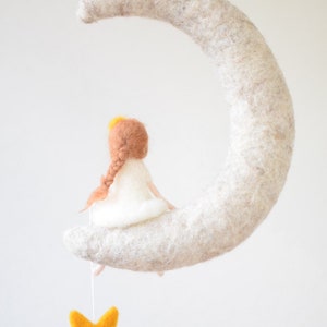 May include: A felt moon mobile with a small felt girl sitting on it. The girl has brown hair and a white dress. A yellow felt star hangs from the moon.