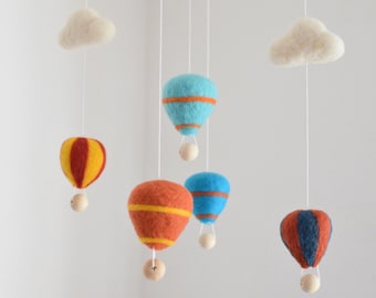 May include: A felt mobile with five hanging elements: two white clouds, three hot air balloons in blue, red, and orange with yellow stripes, and wooden beads.