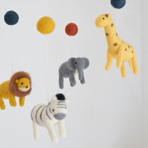 Peut inclure: Un mobile bébé en feutre avec une girafe jaune, un éléphant gris, un zèbre blanc, un lion jaune et des boules de feutre colorées.