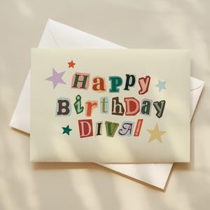 May include: A cream-colored birthday card with the words "Happy Birthday Diva!" in a colorful, cut-out style. The card is decorated with star shapes in various colors and is placed on top of a white envelope.