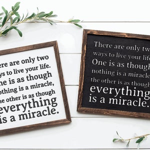 May include: Two wooden signs with a white background and black text. The text on both signs reads: "There are only two ways to live your life. One is as though nothing is a miracle, the other is as though everything is a miracle."