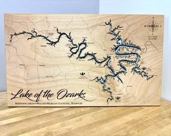 May include: A wooden map of Lake of the Ozarks, Missouri. The map is laser cut and shows the outline of the lake with its many coves and inlets. The map is mounted on a wooden plaque and includes the text "Lake of the Ozarks" and "BENTON-CAMDEN-MILLER-MORGAN COUNTIES, MISSOURI".