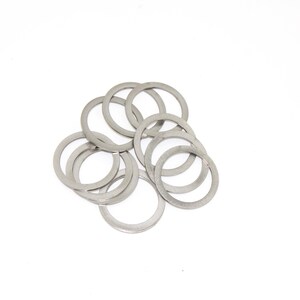 Puede incluir: Un conjunto de arandelas circulares de color plateado. Las arandelas están dispuestas en un montón suelto sobre un fondo blanco. Las arandelas parecen ser de metal y tienen un tamaño y forma uniformes.