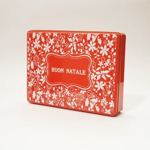 Puede incluir: Lata de metal roja con un diseño floral blanco y las palabras "BUON NATALE" en una pancarta blanca.
