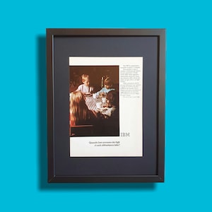 May include: Framed vintage advertisement featuring a family at a table. The ad includes the IBM logo and text in Italian. The image is set against a blue background, with a black frame and a dark blue mat.