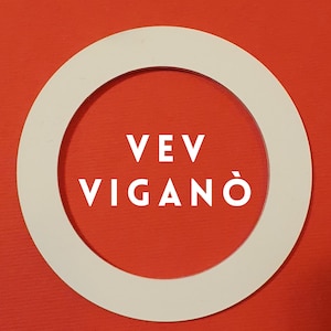 Könnte beinhalten: Weißer Kreis mit einem weißen Ring darum. Der Text "VEV VIGANÓ" befindet sich in der Mitte des Kreises.