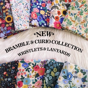 May include: A collection of colourful fabric swatches featuring floral patterns. The fabrics are arranged in a semi-circle with the text "*NEW* BRAMBLE & CURIO COLLECTION WRISTLETS & LANYARDS" in black text at the bottom.