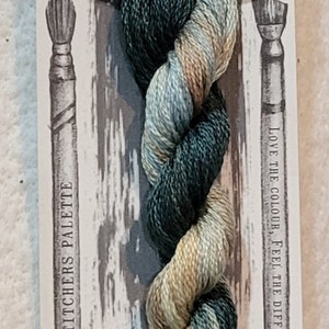 Peut inclure: Une pelote de fil à broder dans des tons de vert, bleu et beige. Le fil est étiqueté "Rolling Stone" et fait partie de la collection "Stitchers Palette". L'étiquette indique également "Love the color, feel the difference."