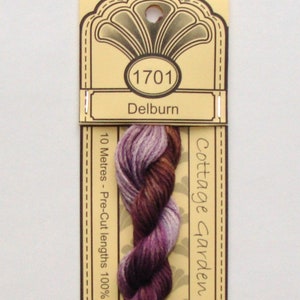 May include: A skein of Cottage Garden Thread in color Delburn, number 1701. The thread is a blend of purple, brown, and lavender hues. The label reads "10 Metres - Pre-Cut lengths 100% Cotton - 6 S".