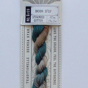 May include: A skein of hand-dyed stranded cotton embroidery floss in shades of brown, green, and gray. The floss is labeled "Bois d'If" and is 10 meters long. The label also says "Traditionelle Brenda Ryan" and "CG Hand Dyed".
