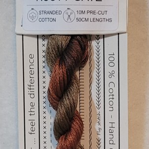 May include: Stranded cotton embroidery floss in shades of brown and olive green, labeled "Rusty Gate." The label includes the brand logo, product details, and text: "Love the colour... feel the difference."