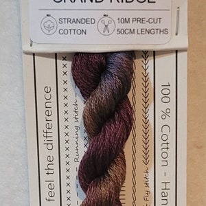 May include: A skein of stranded cotton embroidery floss in shades of burgundy, brown, and gold. The label reads "No. 411 GRAND RIDGE" and includes text about the cotton and pre-cut lengths. The floss is 100% cotton and hand-dyed in Australia.