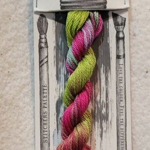 May include: A skein of hand-dyed embroidery floss in shades of green, pink, and purple. The floss is labeled "Sprinkles" and "Hand Dyed".