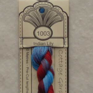May include: A skein of embroidery floss in shades of blue, red, and purple. The floss is labeled "1003 Indian Lily" and "Cottage Garden".