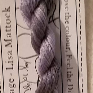 May include: A skein of Cineraria stranded cotton thread, pre-cut to 10 meters. The thread is a blend of gray and lavender, with the text "Love the colour, Feel the Difference" visible on the packaging. The brand is Forage - Lisa Mattock.