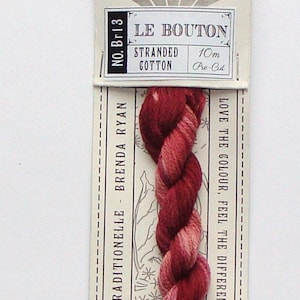 May include: A skein of Le Bouton stranded cotton thread in shades of red and pink. The label reads "STRANDED COTTON" and "10m Pre-Cut". The packaging includes the text "TRADITIONELLE - BRENDA RYAN" and "LOVE THE COLOUR, FEEL THE DIFFERENCE".