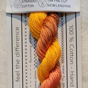 Pode incluir: Um pacote de fio de bordado tingido à mão em tons de laranja e amarelo. O fio é etiquetado como "VD 05 Ginger Lily" e é 100% algodão. Vem em comprimentos pré-cortados de 10 metros de 50 centímetros cada. O rótulo também diz "Love the color... feel the difference".