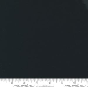 May include: Plain black fabric with a ruler along the bottom edge. The fabric is a deep, dark shade of black. The ruler is white with black markings and the word "moda" printed on it.