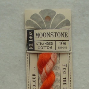 May include: A skein of Moonstone stranded cotton thread, pre-cut to 10 meters. The label features the number 1402 and text. The thread is a blend of orange and light pink. The label has a decorative fan design.