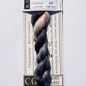 May include: A skein of India stranded cotton thread, pre-cut to 10m. The thread is a blend of gray, black, and tan colors. The label reads "India" and "CG Hand Dyed". The packaging has a decorative, scalloped edge.