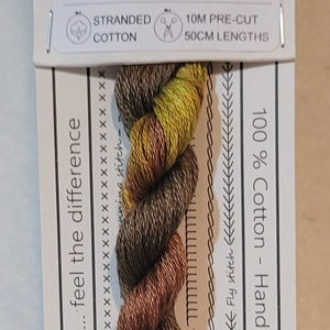 Può includere: Un gomitolo di filo da ricamo in cotone River Gum, n. 203, con una miscela di tonalità marrone, rame e verde-giallo. L'etichetta include informazioni sul prodotto, tra cui 100% cotone e tinto a mano in Australia.