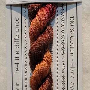 Pode incluir: Um novelo de linha de bordar de algodão torcido em VD 06 Gaillarde. A linha é uma mistura de tons castanhos, laranja e vermelhos. O rótulo diz "100% Algodão - Tingido à mão na Austrália".