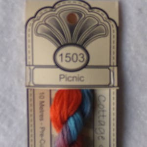 May include: A skein of embroidery floss in shades of orange, blue, and purple. The floss is labeled "Cottage Garden" and "1503 Picnic".
