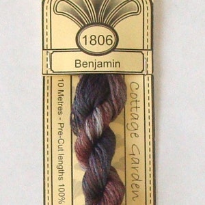 May include: A skein of Cottage Garden Threads embroidery floss, color "Benjamin" (1806). The thread is a blend of dark red, purple, and white. The label is tan with the brand name and product information.
