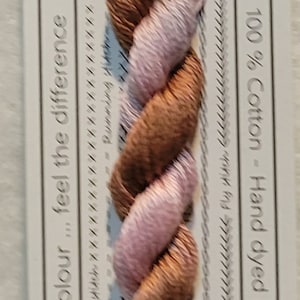 Pode incluir: Fio de bordar de algodão torcido na cor Begonia, VD 26. O fio apresenta tons de castanho e rosa, pré-cortado em comprimentos de 10 metros. O rótulo indica 100% algodão e tingido à mão na Austrália.