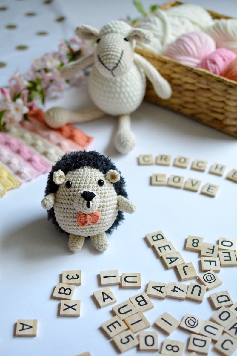May include: A crocheted hedgehog with a black nose and a pink bow tie, a crocheted sheep, and wooden letter tiles spelling "CROCHE LOVE" and other letters and numbers.